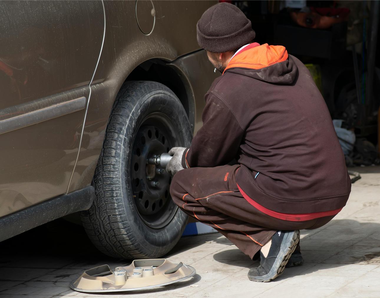 Mechanic examining car's undercarriage at a garage, focusing on vehicle maintenance.