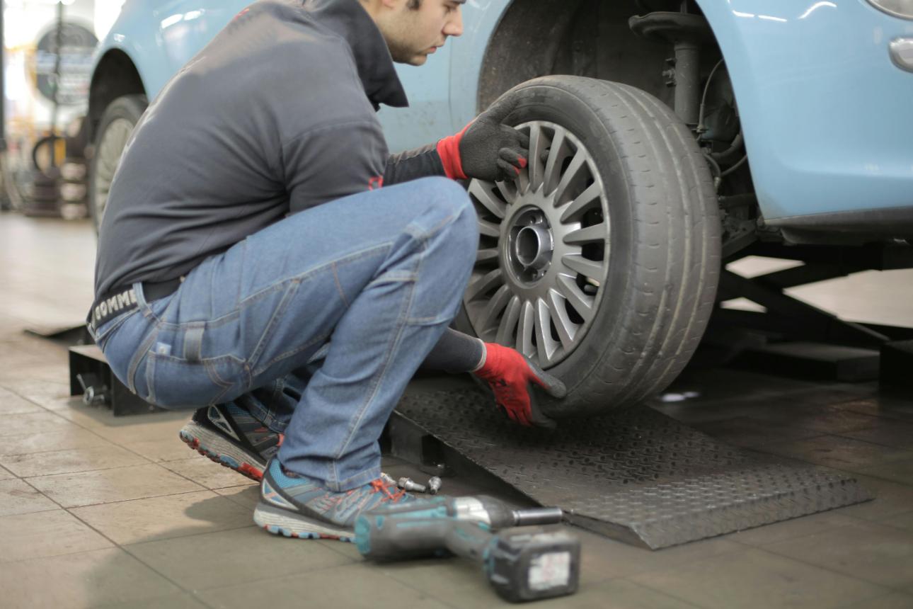 Mechanic examining car's undercarriage at a garage, focusing on vehicle maintenance.